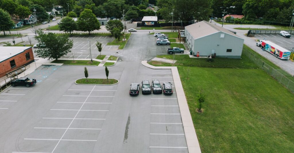 Drone shot of a parking lot in Chattanooga with cars and buildings, surrounded by lush greenery.